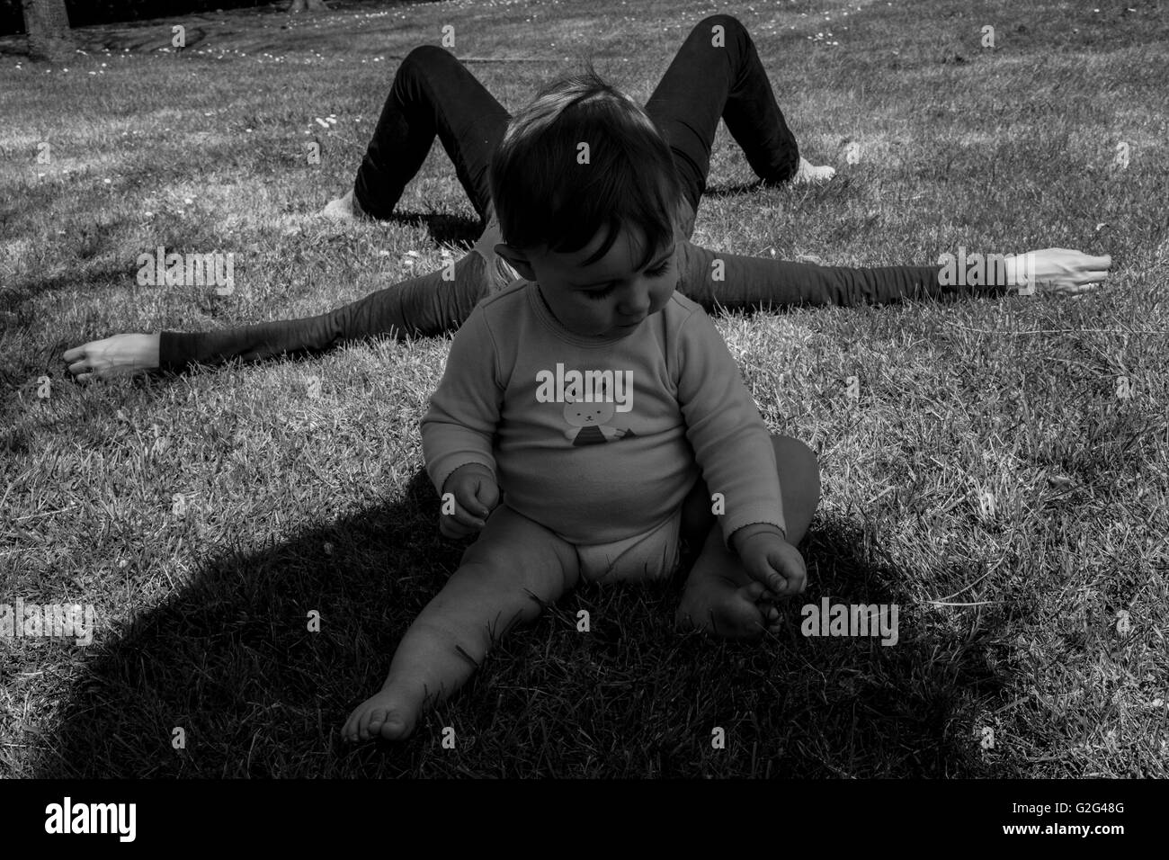 Baby Boy spielt auf Boden im Schatten mit Mutter Verlegung auf dem Rasen im Hintergrund Stockfoto