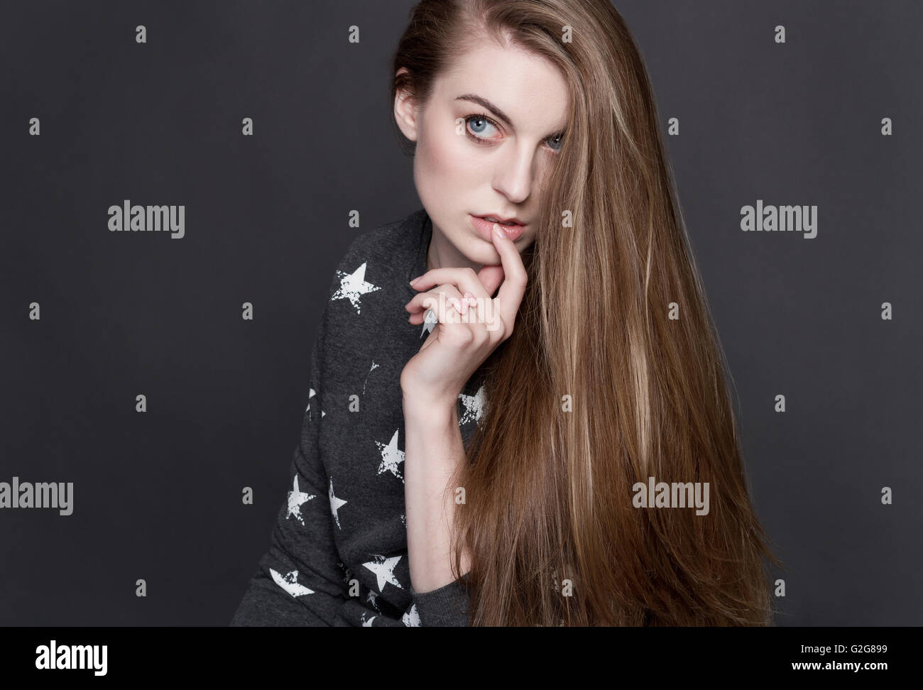 Eine schüchterne junge blonde Mädchen in einen grauen Pullover. Sie berührt sinnlich ihre Lippen mit seinen Fingern. Sie ist intelligent und neugierig. Ihr Luxur Stockfoto