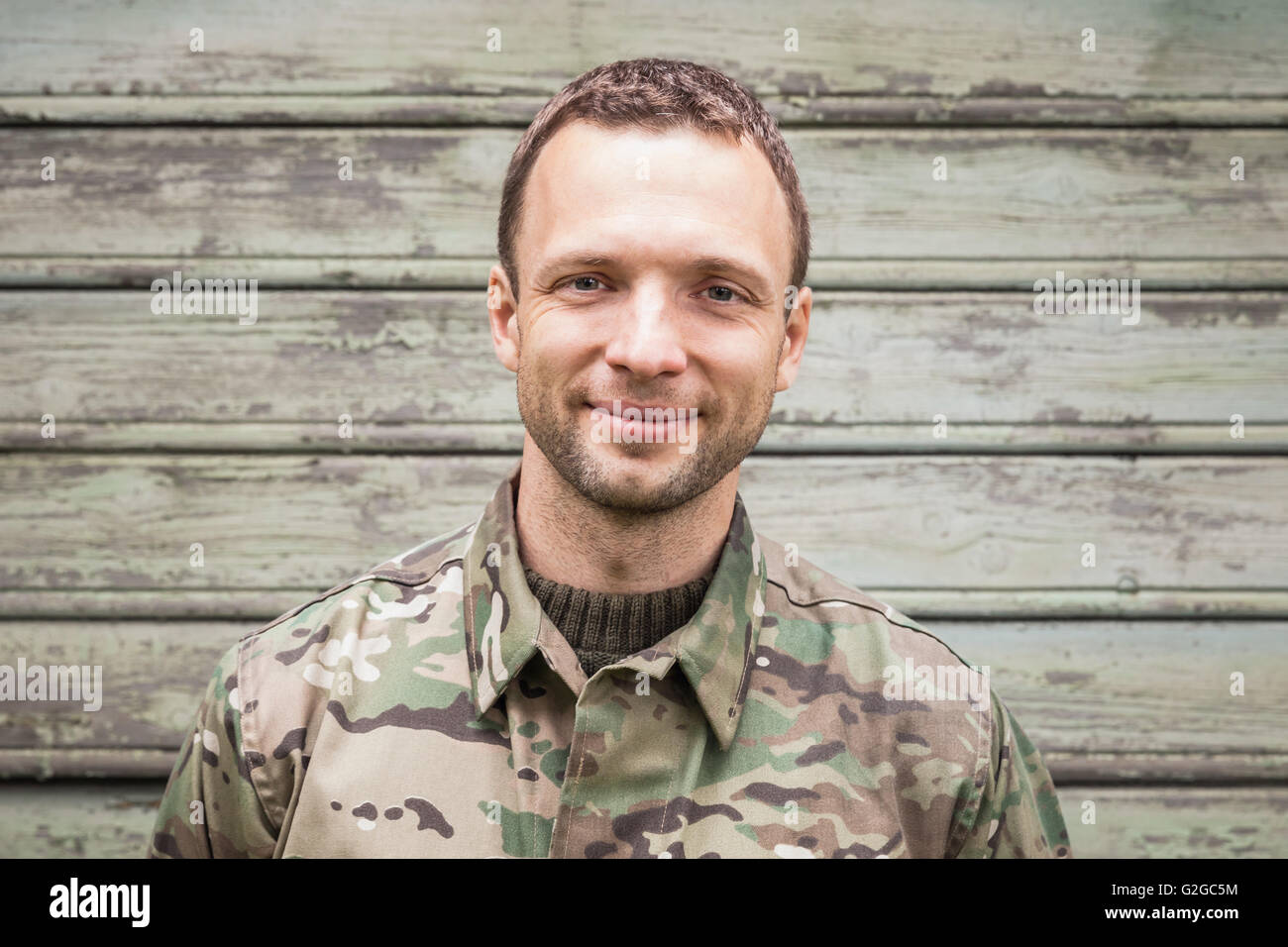 Lächelnde kaukasischen Jüngling in militärischen Tarnuniform. Outdoor Closeup Portrait über grüne ländliche Holzwand Stockfoto