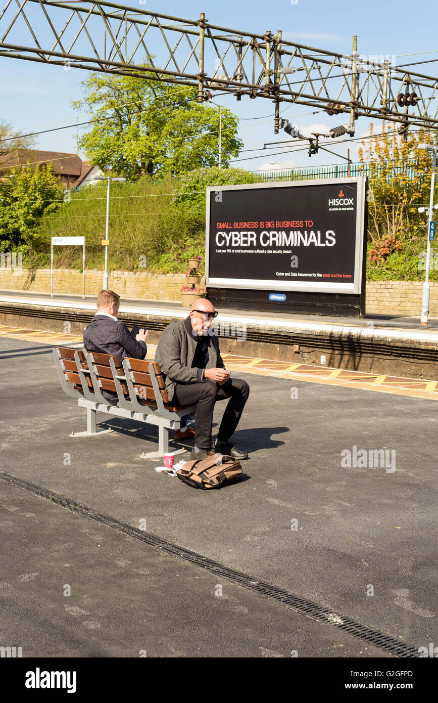 Zwei Pendler, die mit ihrer Telefone mit einem Cyberkriminellen Plakat im Hintergrund sitzen Stockfoto