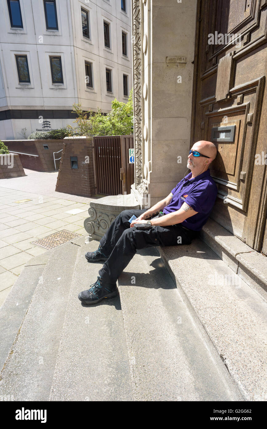 Haded Glatzkopf sitzt und entspannt in der Sonne draußen Chelmsford County Court Essex England Stockfoto