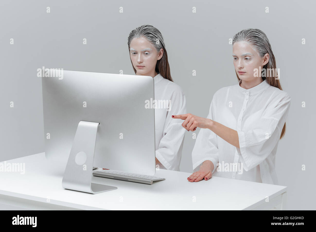 Zwei kosmischen Damenmode vor dem Computer sitzt. Mädchen Zeigefinger auf dem Bildschirm über grauen Hintergrund Stockfoto