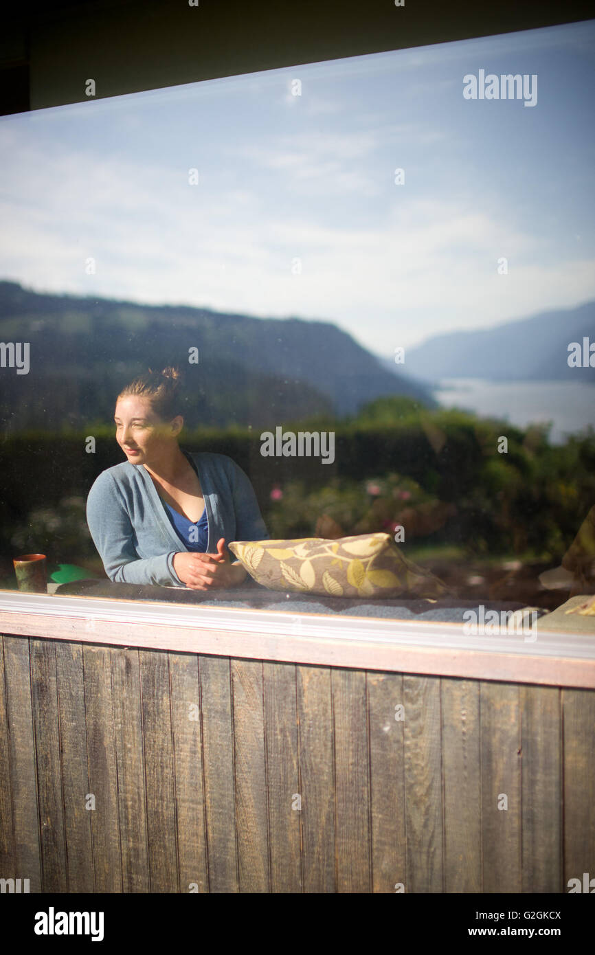 Junge Erwachsene Frau suchen aus Fenster, Blick von außen Stockfoto