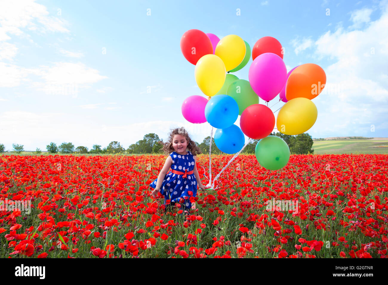 Fröhliches kleines Mädchen mit vielen bunten Luftballons in Rot Blumen Feld Stockfoto