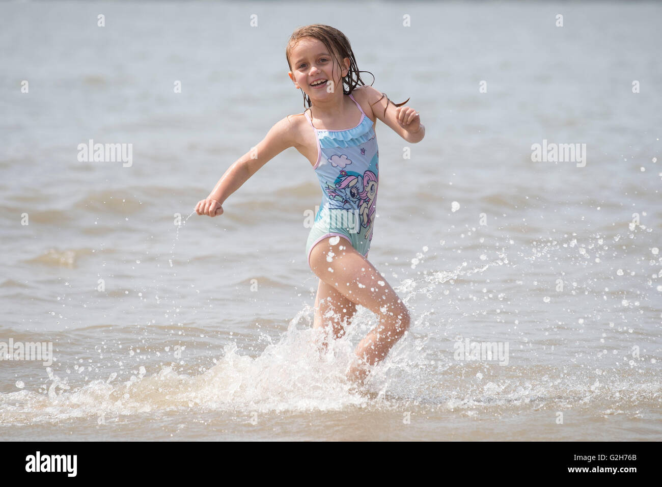 Eine Mädchen spielt, Spritzer und kühlt sich im Meer bei schönem sonnigen Wetter Whitmore Bay, Barry, Wales. Stockfoto