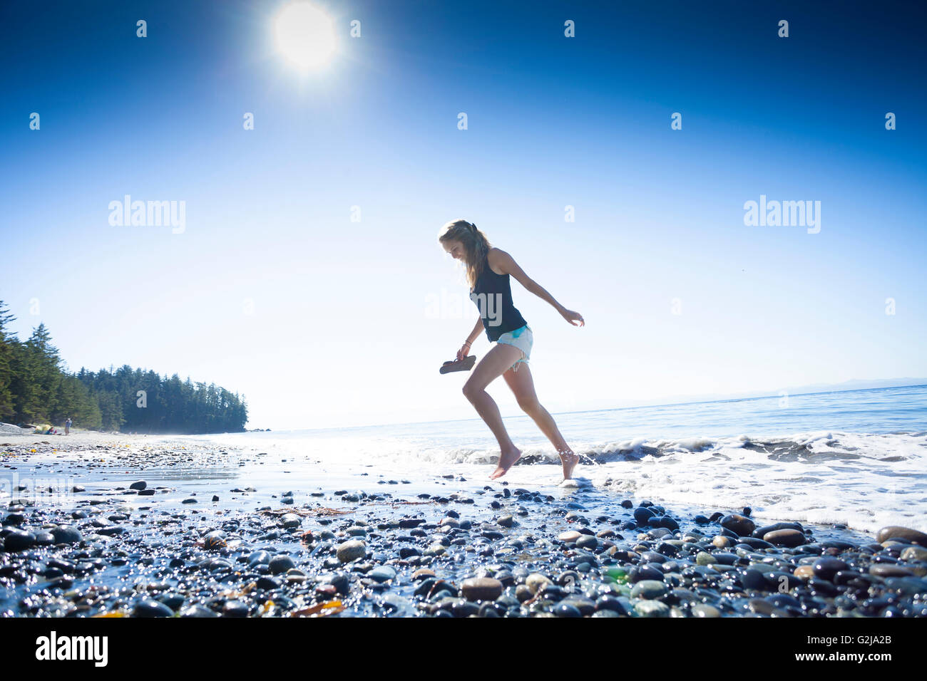 Eine junge Frau läuft barfuß durch die Ufer-Wellen am französischen Beach Provincial Park. Vancouver Island, BC, Kanada. Stockfoto