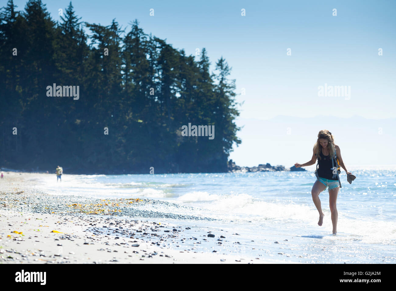 Eine junge Frau in Einzelschritten die Wellen am französischen Beach Provincial Park. Vancouver Island, BC, Kanada. Stockfoto