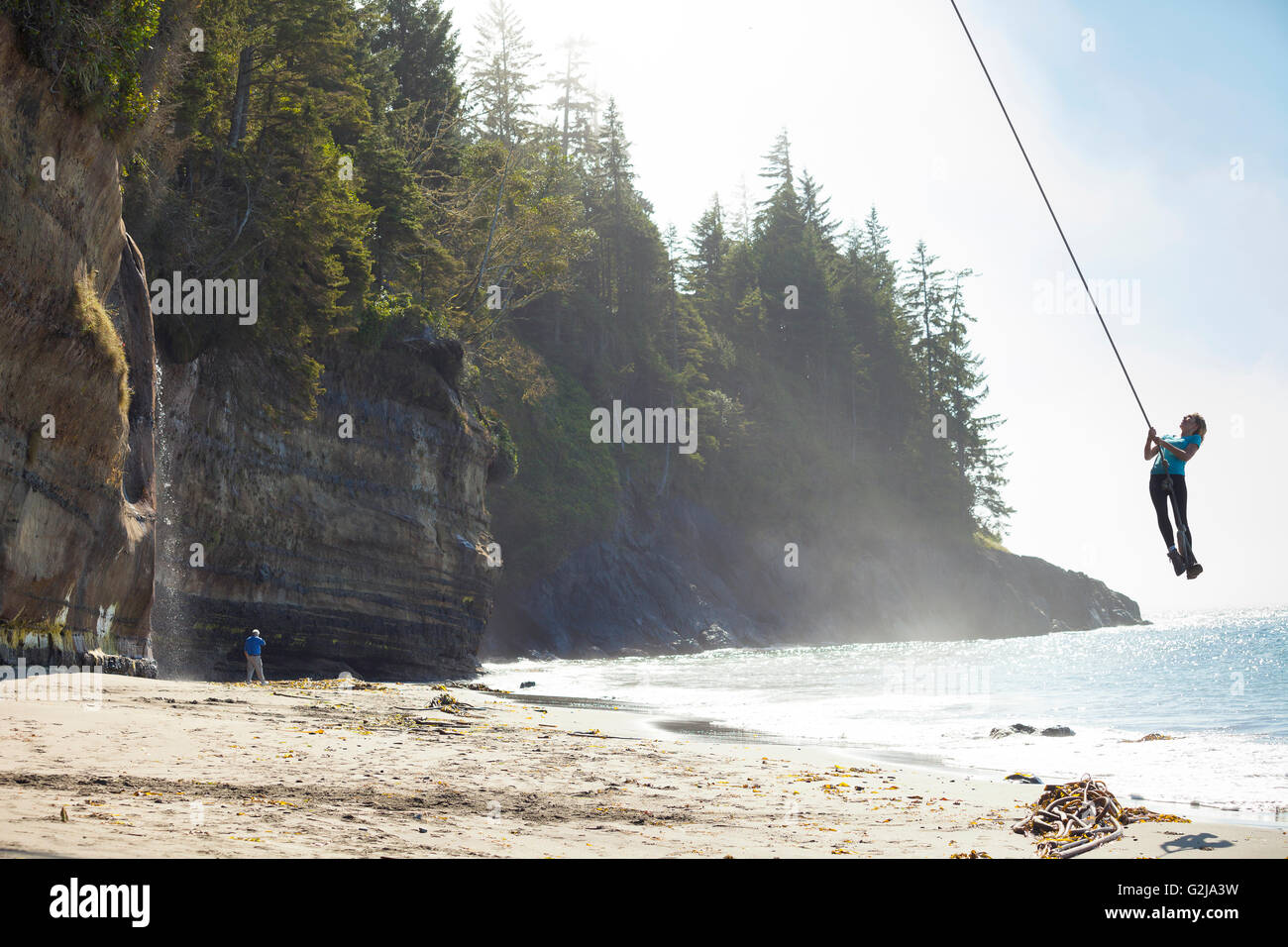 Eine junge Frau schwingt auf einem Seil schwingen im Mystic Beach entlang der Juan de Fuca Trail. Vancouver Island, BC, Kanada Stockfoto