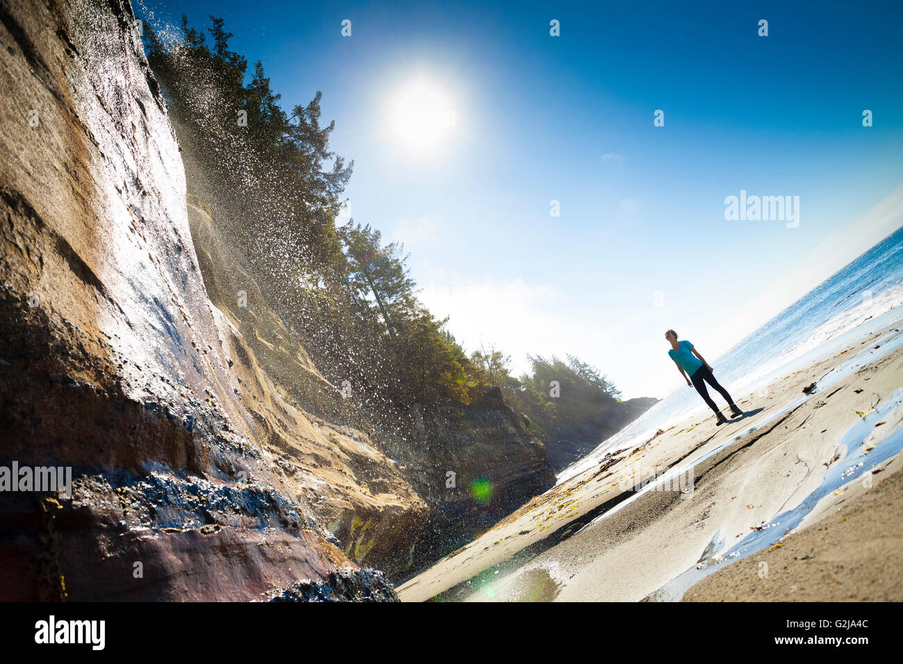 Eine junge Frau unter Wasserfall im Mystic Beach entlang der Juan de Fuca Trail. Vancouver Island, BC, Kanada. Stockfoto