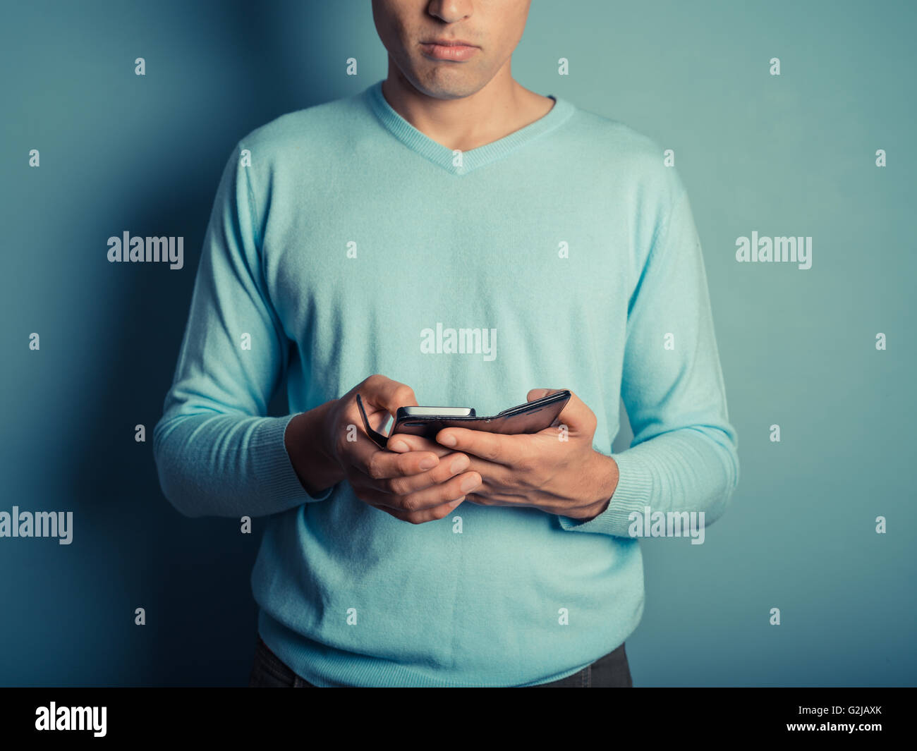 Ein junger Mann trägt einen blauen Pullover ist ein smart Phone verwenden. Stockfoto