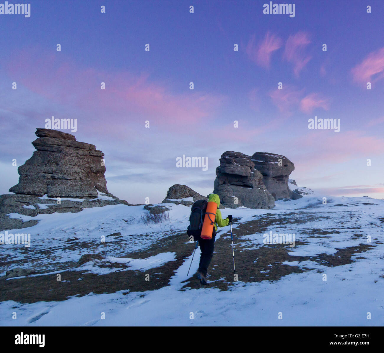 Mann mit Rucksack und Polen gehen in die Berge und Felsen Schnee bedeckten bei lila Sonnenuntergang Stockfoto