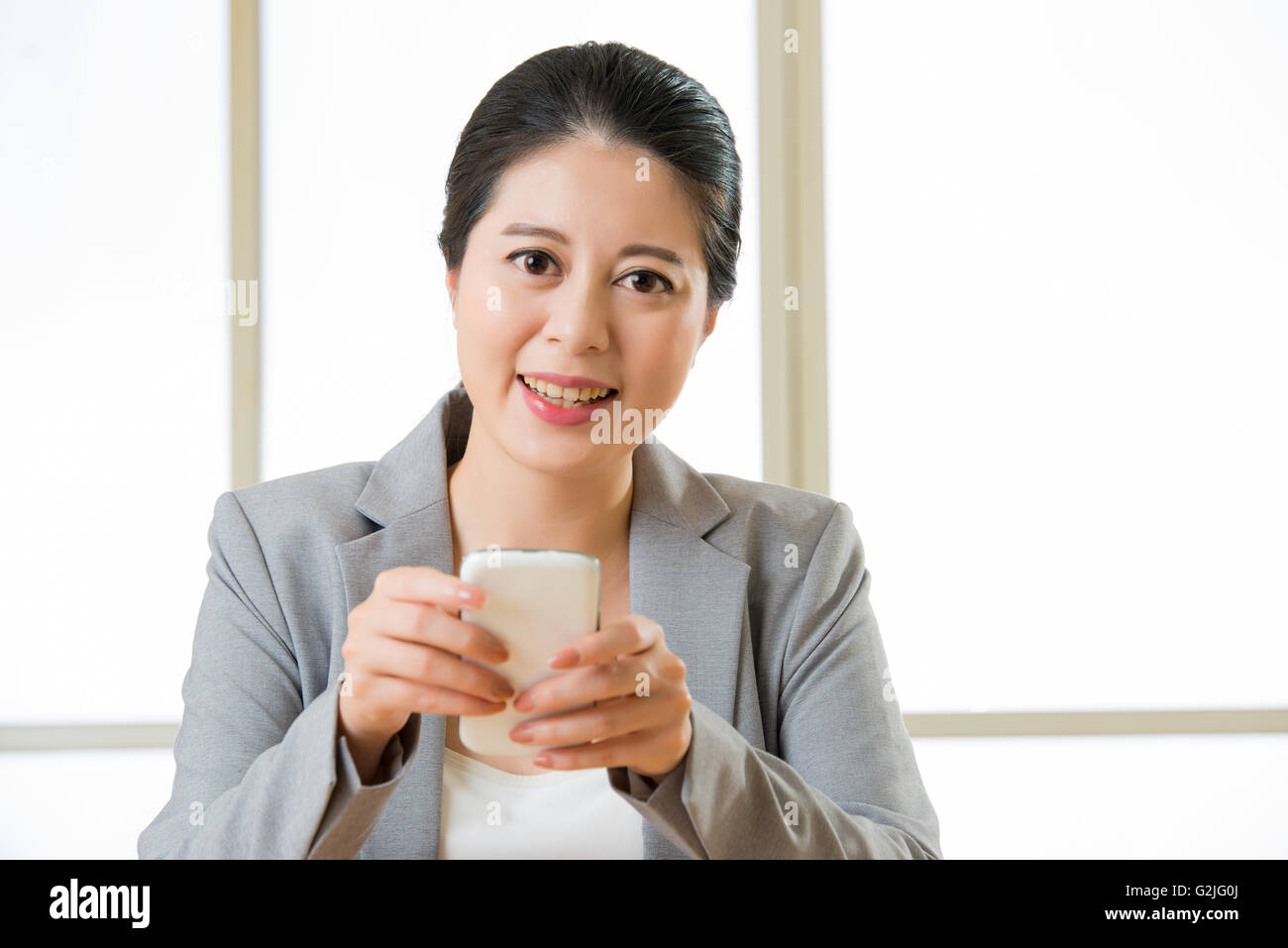 Schöne asiatische Frau lächelnd und mit Smartphone-Textnachrichten im Büro Stockfoto