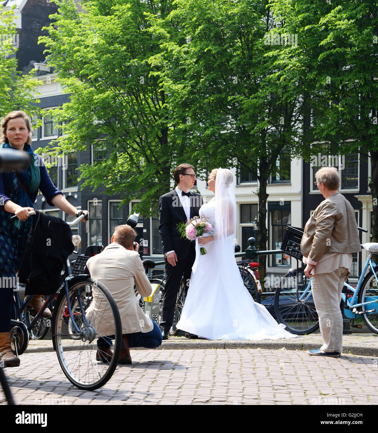 Bester Mann schaut zu, wie frisch verheiratetes Paar für Foto auf Amsterdam Brücke darstellen.  Lady-Zyklen hinter der Szene. Stockfoto