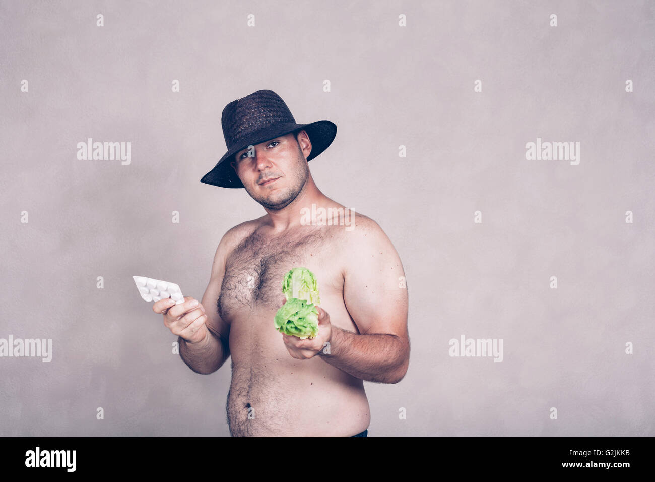 Nackte korpulente Mann mit Hut, die Abhaltung von pharmazeutischen Produkten und Salat. Stockfoto