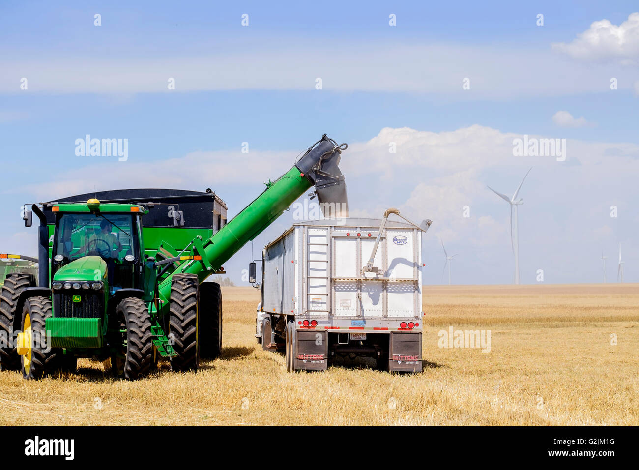Ein Mann fährt ein John Deere Traktor und Brent Getreide Wagen wird Weizen in einem Sattelschlepper in Oklahoma, USA. Stockfoto