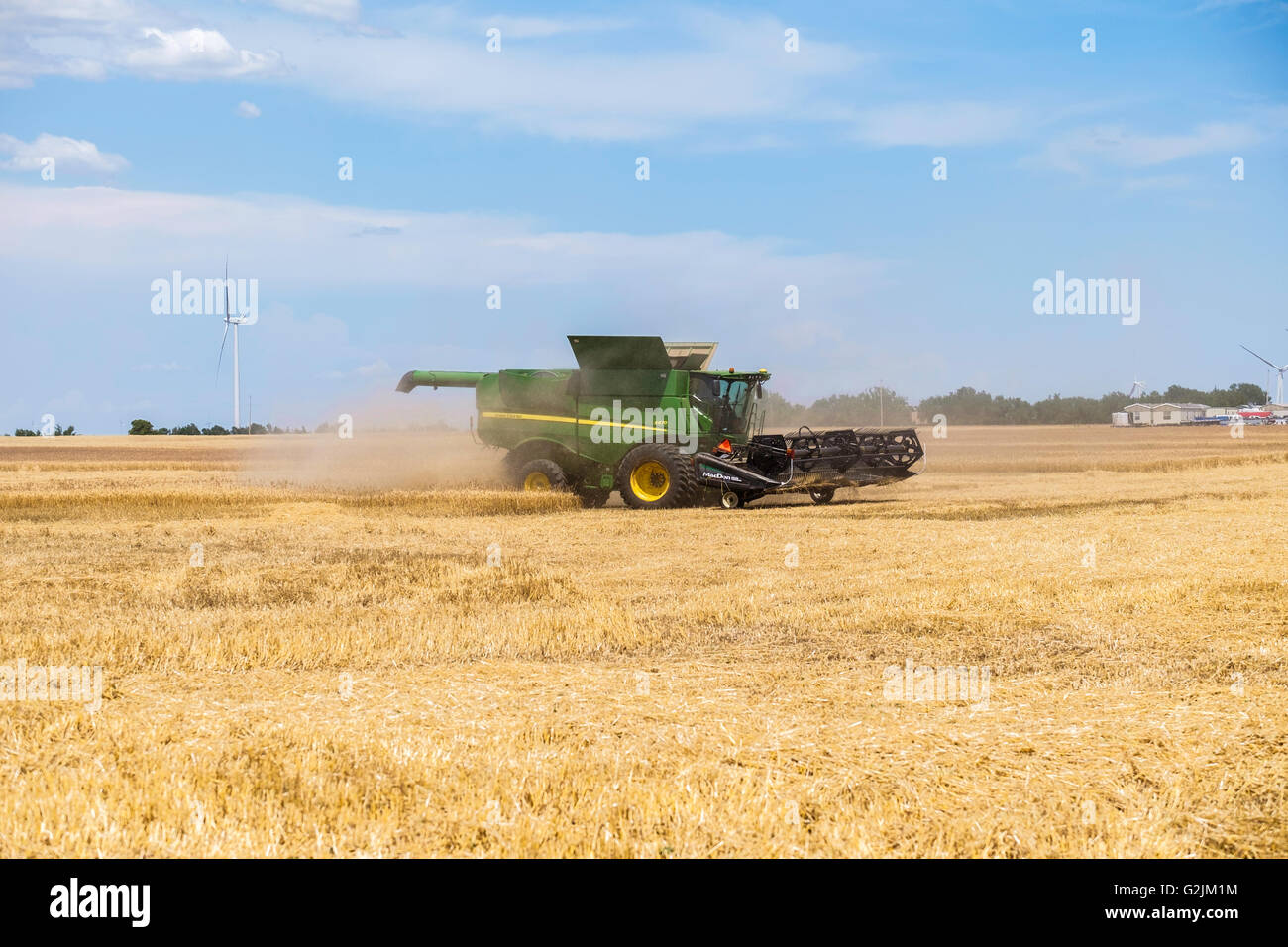 John Deere Mähdrescher erntet Weizen in Oklahoma, USA. Windkraftanlagen sind im Hintergrund. Stockfoto