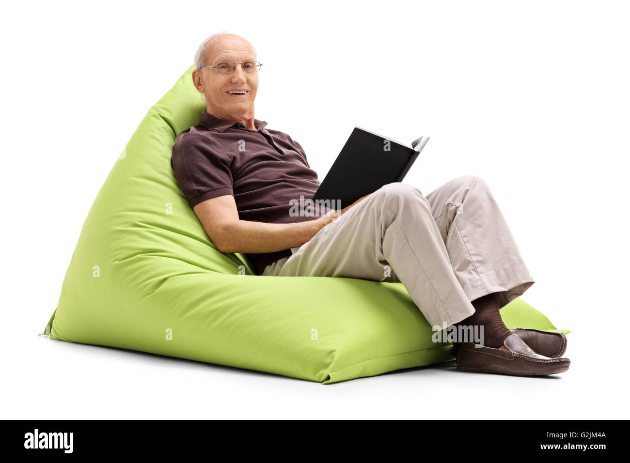 Entspannte senior Mann liest ein Buch sitzend auf einem grünen Sitzsack isoliert auf weißem Hintergrund Stockfoto