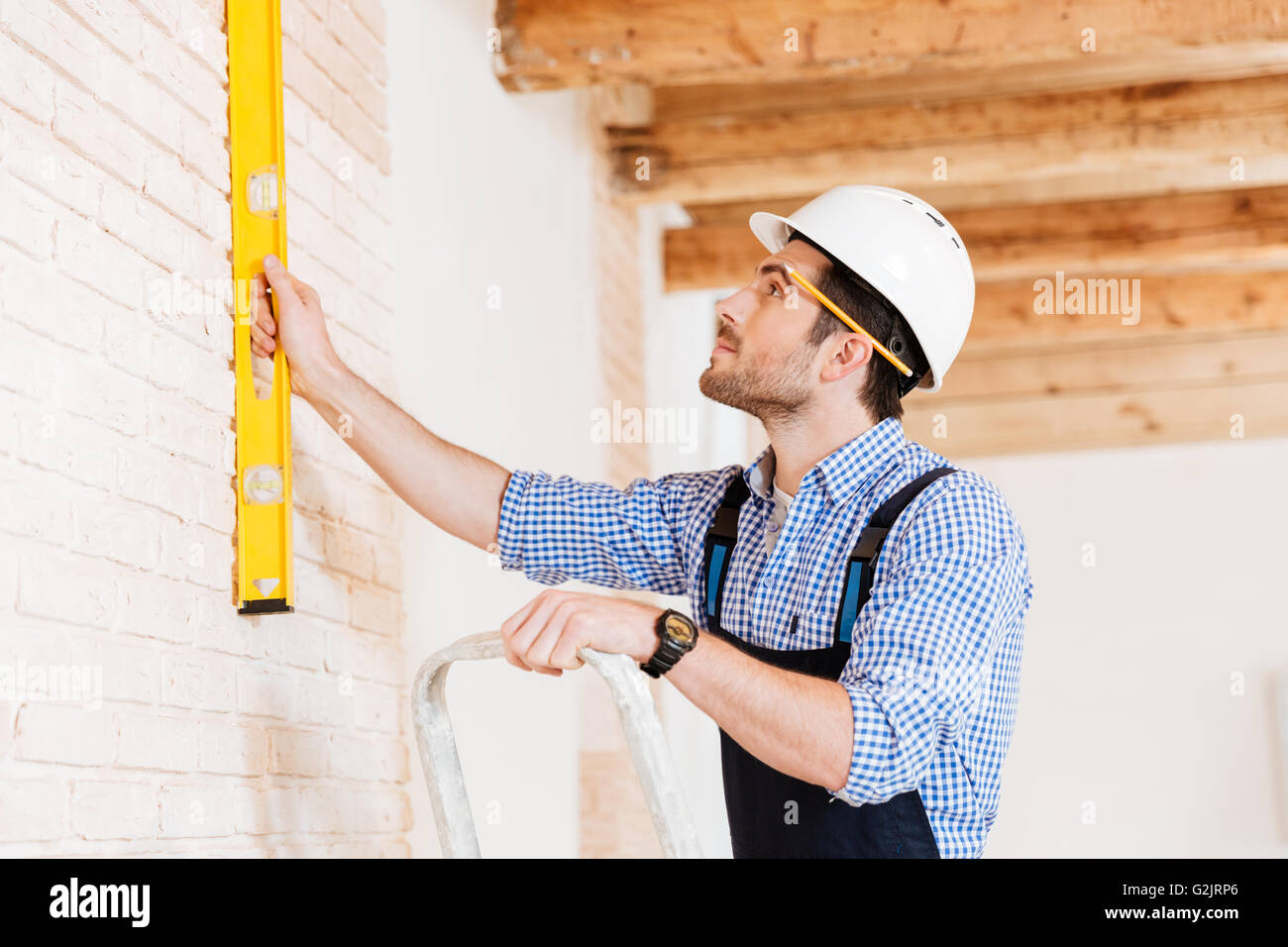 Close-up Portrait eines Erbauers halten Bau Ebene gegen die Wand und auf der Leiter drinnen stehend Stockfoto