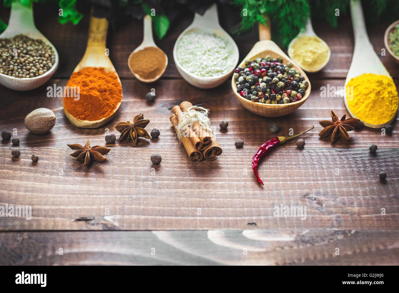 Schöne bunte Gewürze in hölzerne Löffel und Schüsseln mit Salat, Dill und Basilikum auf einem alten Holz- braun Tabelle. freier Speicherplatz für y Stockfoto