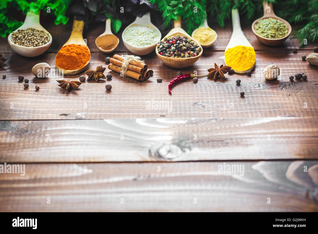 Schöne bunte Gewürze in hölzerne Löffel und Schüsseln mit Salat, Dill und Basilikum auf einem alten Holz- braun Tabelle. freier Speicherplatz für y Stockfoto