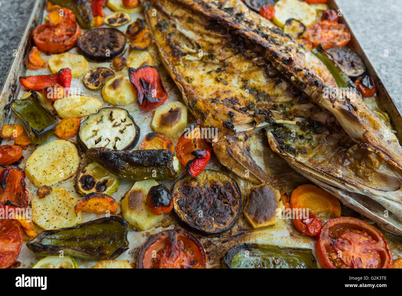 Nahaufnahme von leckeren Fisch gebacken mit gebratenen Tomaten, Kartoffeln und Gemüse Stockfoto