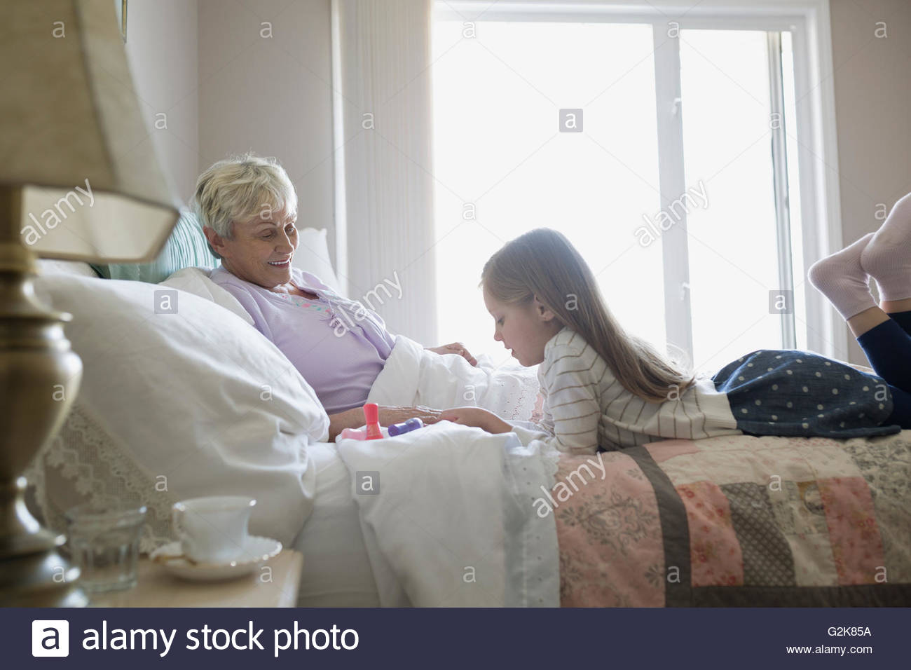 Enkelin geben Großmutter Maniküre im Bett Stockfoto