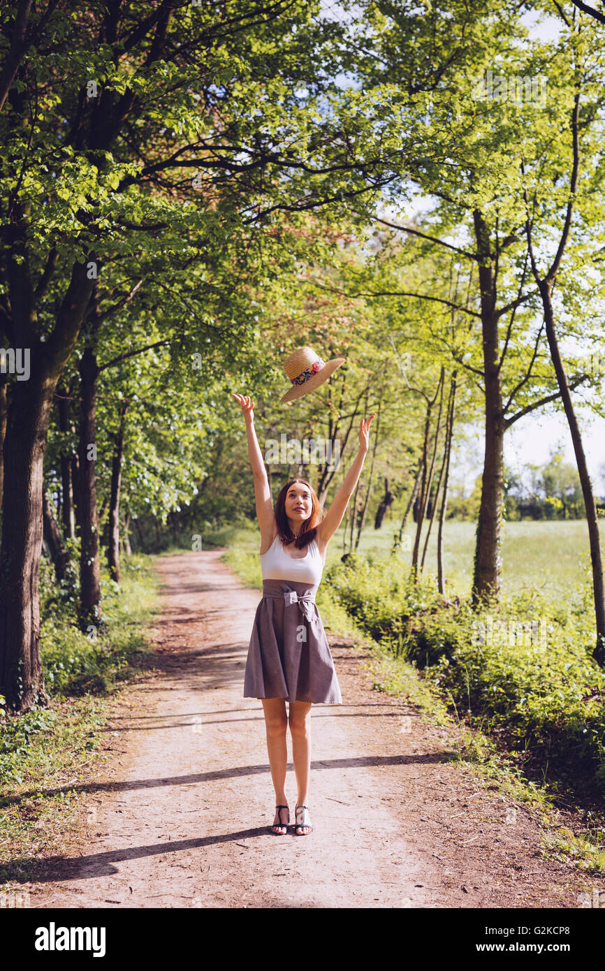 Glückliche junge Frau, die ihren Sommerhut in die Luft werfen Stockfoto