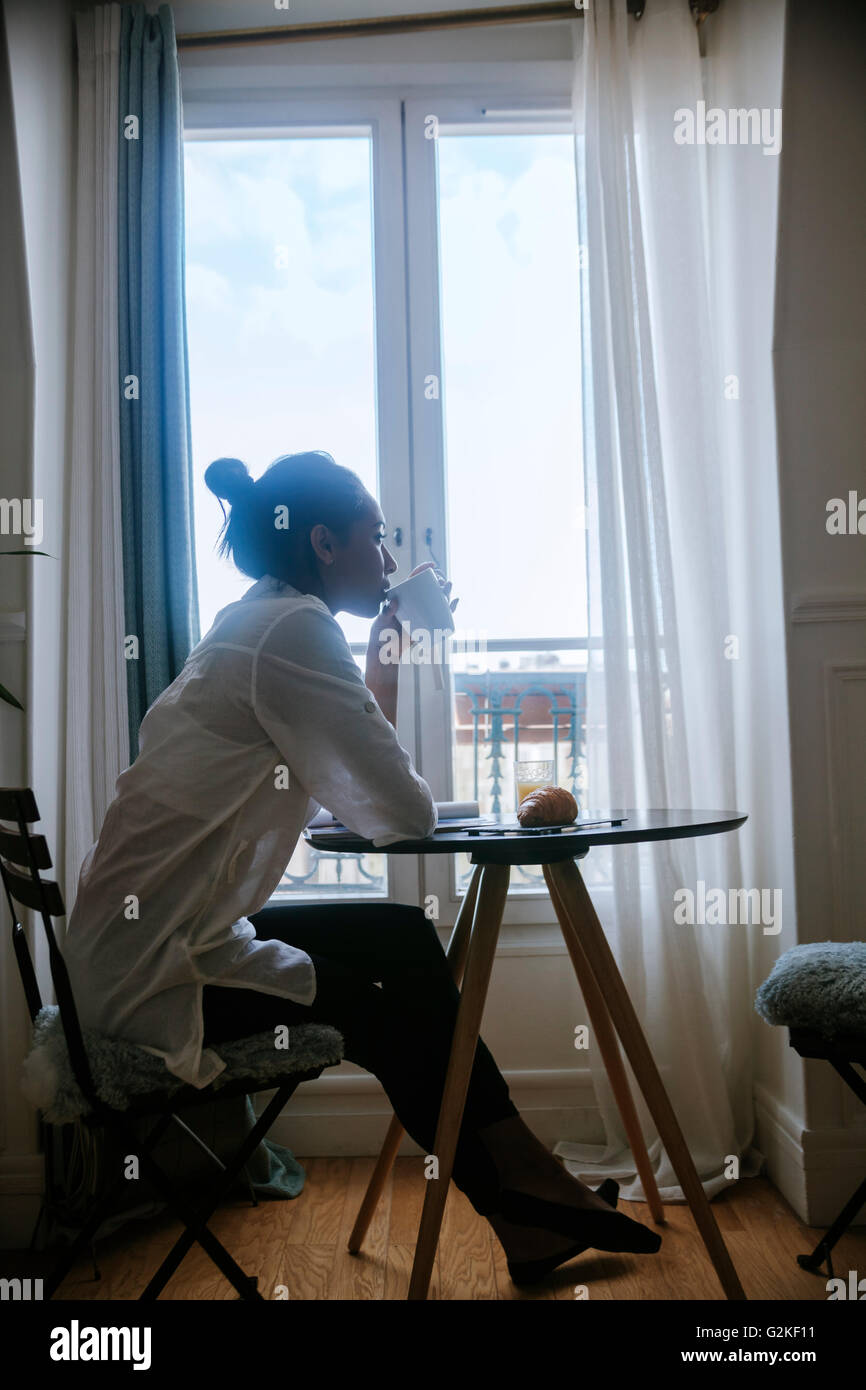 Junge Frau sitzt am Frühstückstisch Kaffee trinken Stockfoto