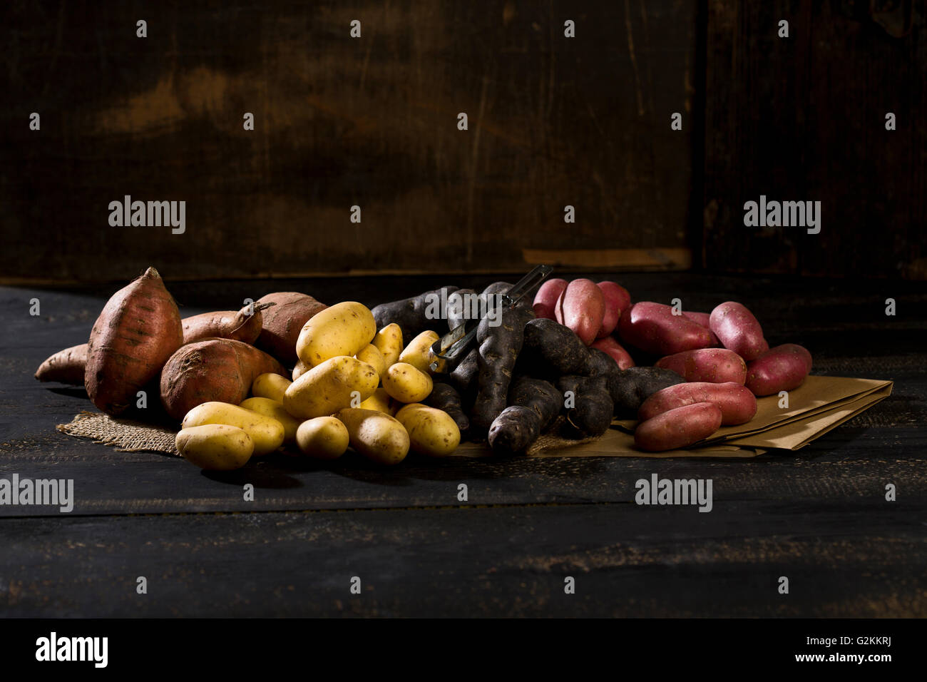 Verschiedene Arten von Kartoffeln auf braunem Papier, Jute und dunkles Holz Stockfoto