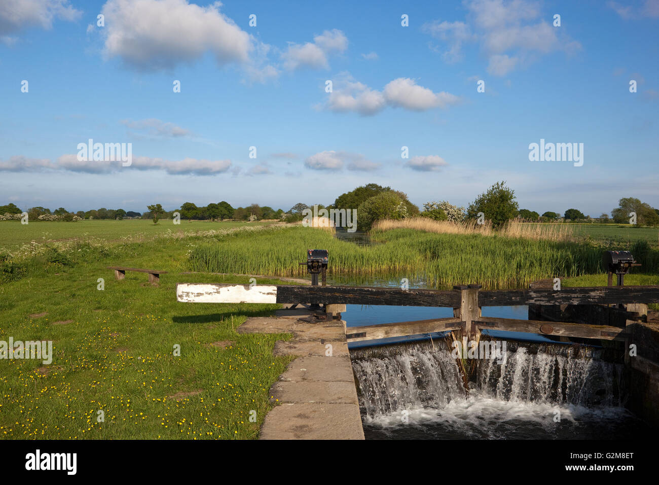 Wasser gießen durch Kanal-Schleusen neben einer ländlichen Leinpfad mit Bänken und Picknick-Bereich in einer Agrarlandschaft im Mai. Stockfoto