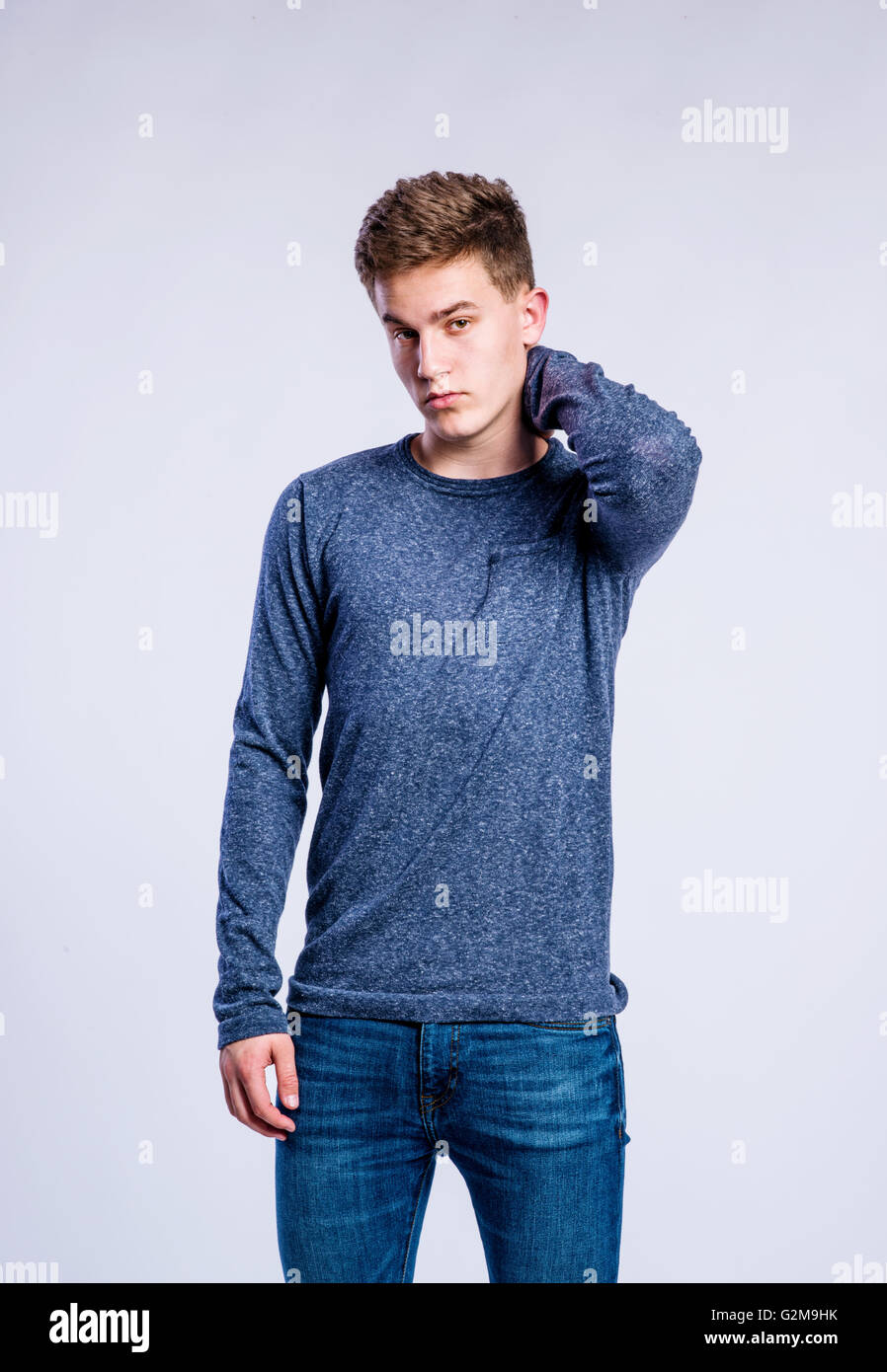 Teenager in Jeans und blaues Sweatshirt, junger Mann, Studio gedreht auf grauem Hintergrund Stockfoto
