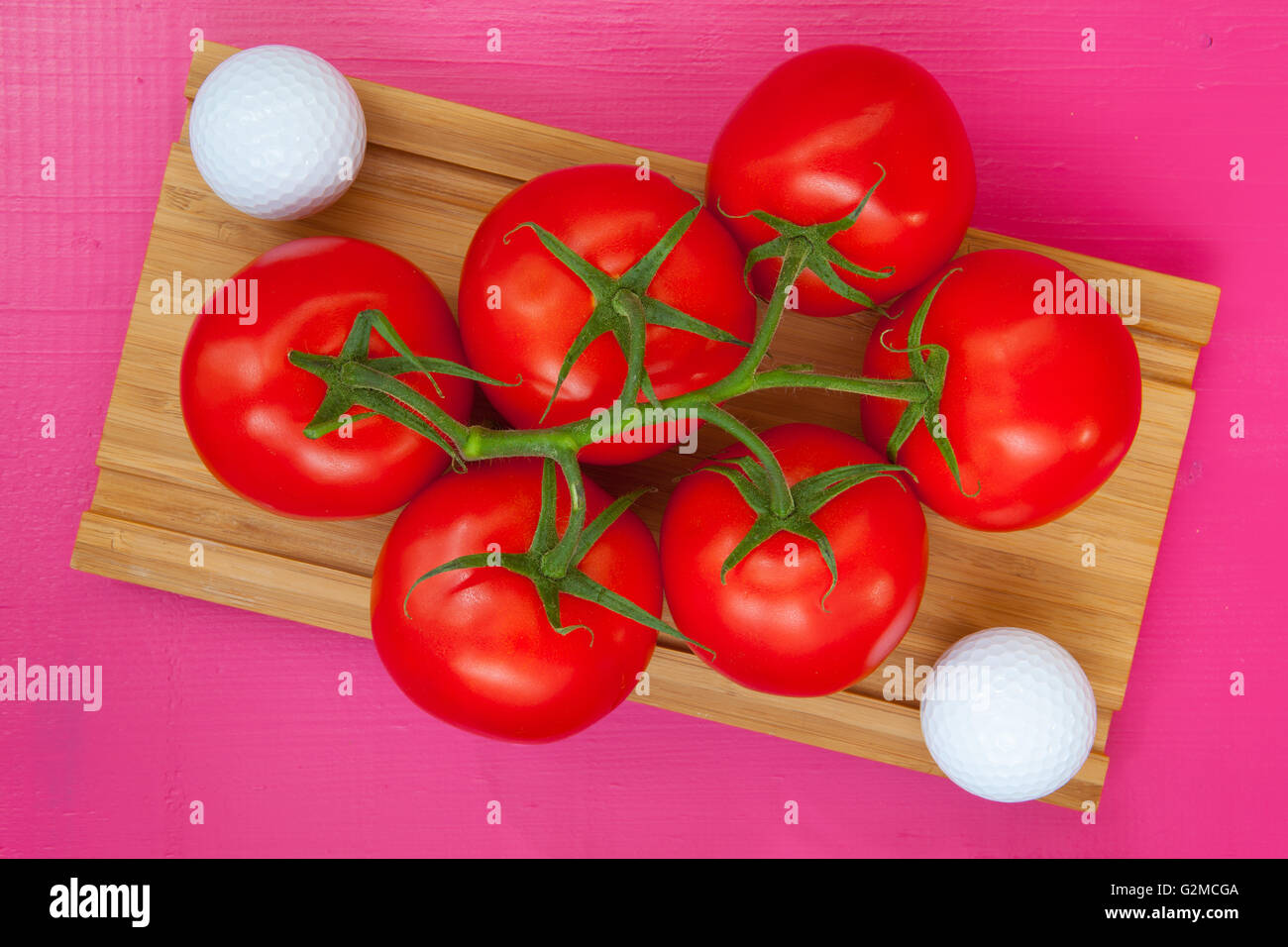 Golf-Frühstück - rote Tomaten und Golfball auf dem Schreibtisch aus Holz Stockfoto