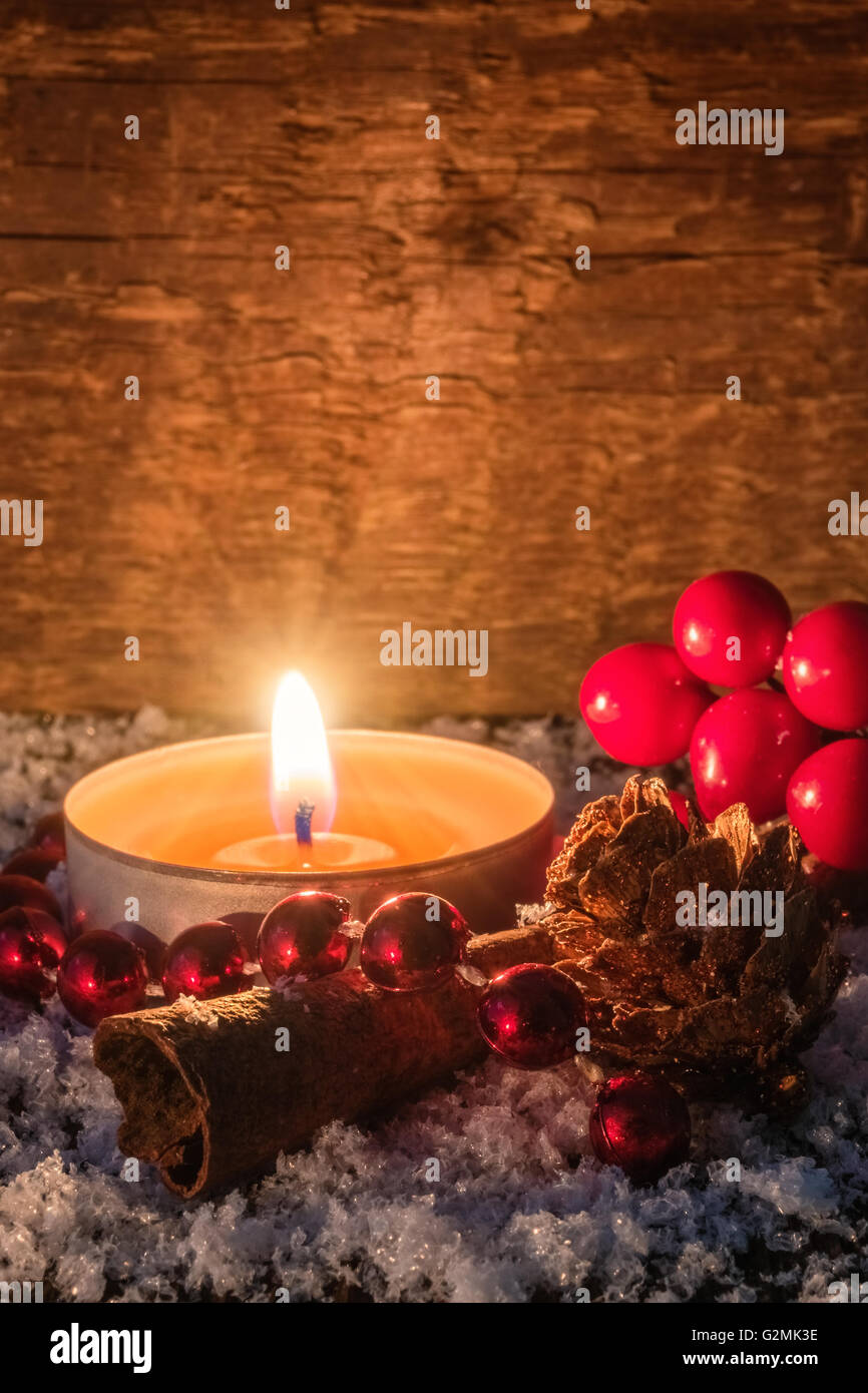 Atmosphärische Weihnachtskarte oder Hintergrund mit brennendem Teelicht, Kerze, Zimt, Tannenzapfen und Preiselbeeren auf einem Holztisch cov Stockfoto