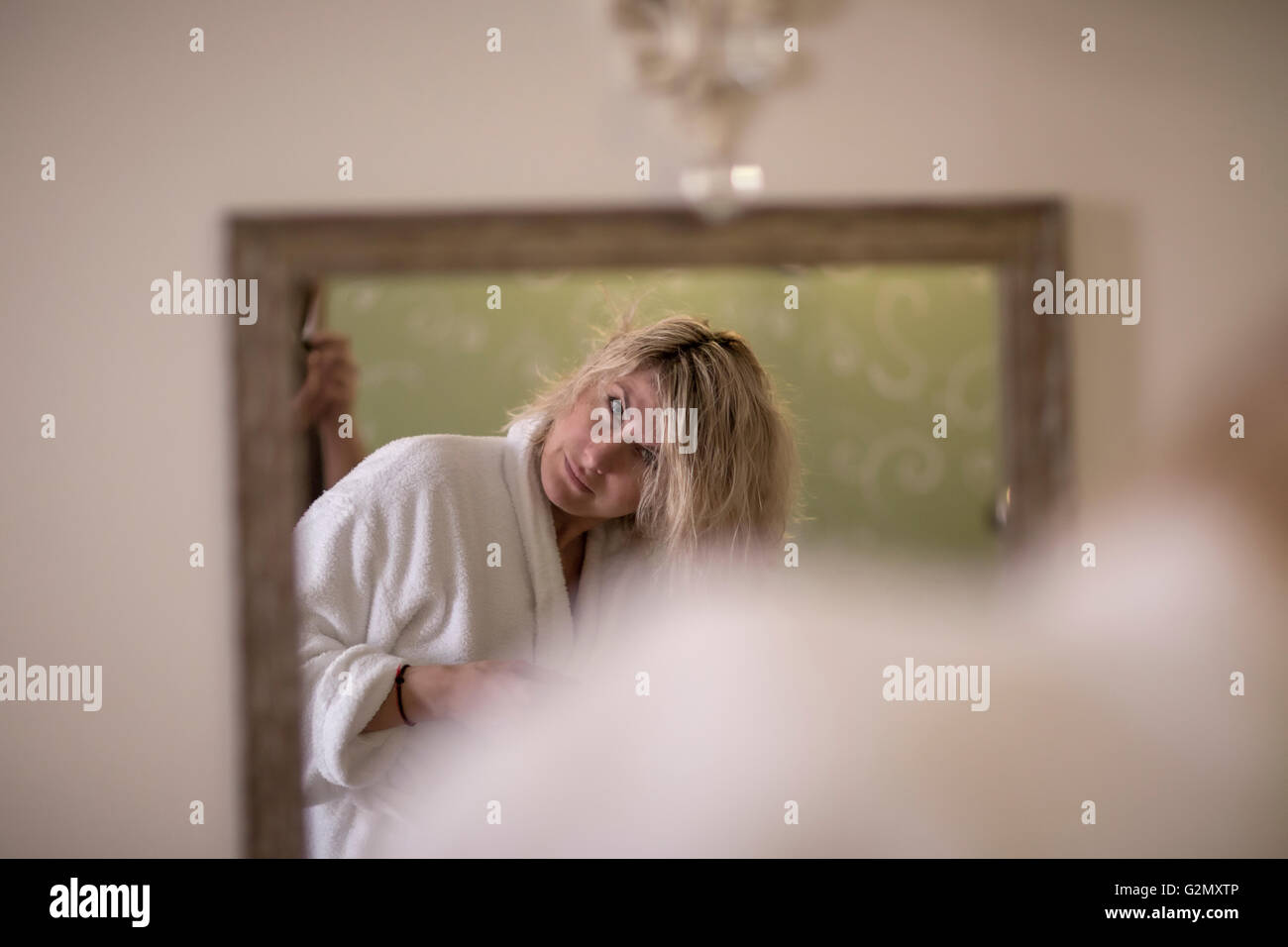 Schöne blonde Frau im Bademantel ist auf der Suche nach sich selbst im Spiegel Stockfoto