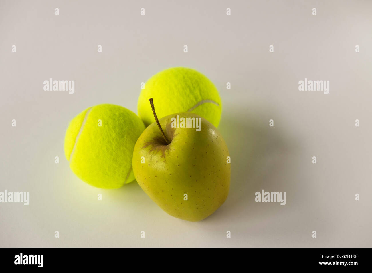 Golden gelber Apfel vor zwei Tennisbälle auf weißem Hintergrund Stockfoto