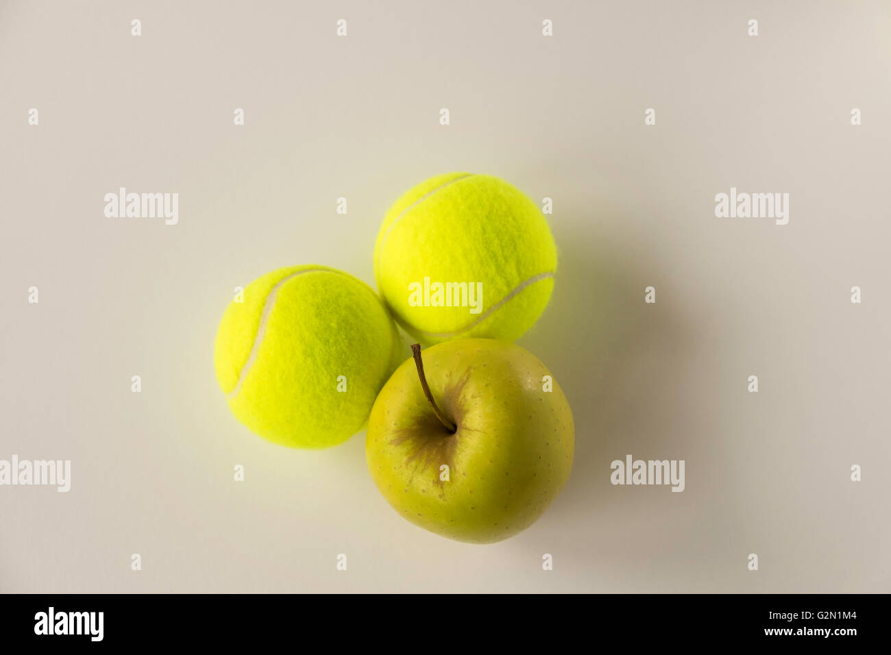 Zwei Tennisbälle mit goldener gelber Apfel auf weißem Hintergrund Stockfoto