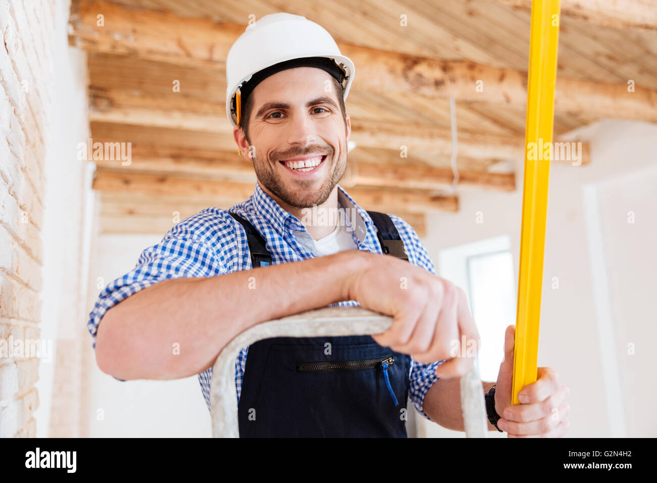 Close-up Portrrait ein Smilling Handwerker auf der Leiter mit einem Niveau stehend Stockfoto