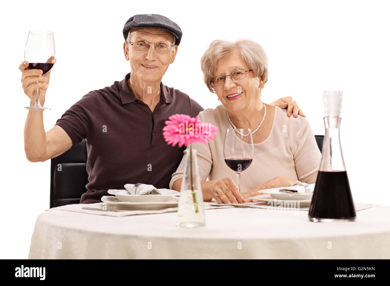 Ältere Mann und Frau posiert sitzen an einem Tisch mit Rotwein isoliert auf weißem Hintergrund Stockfoto