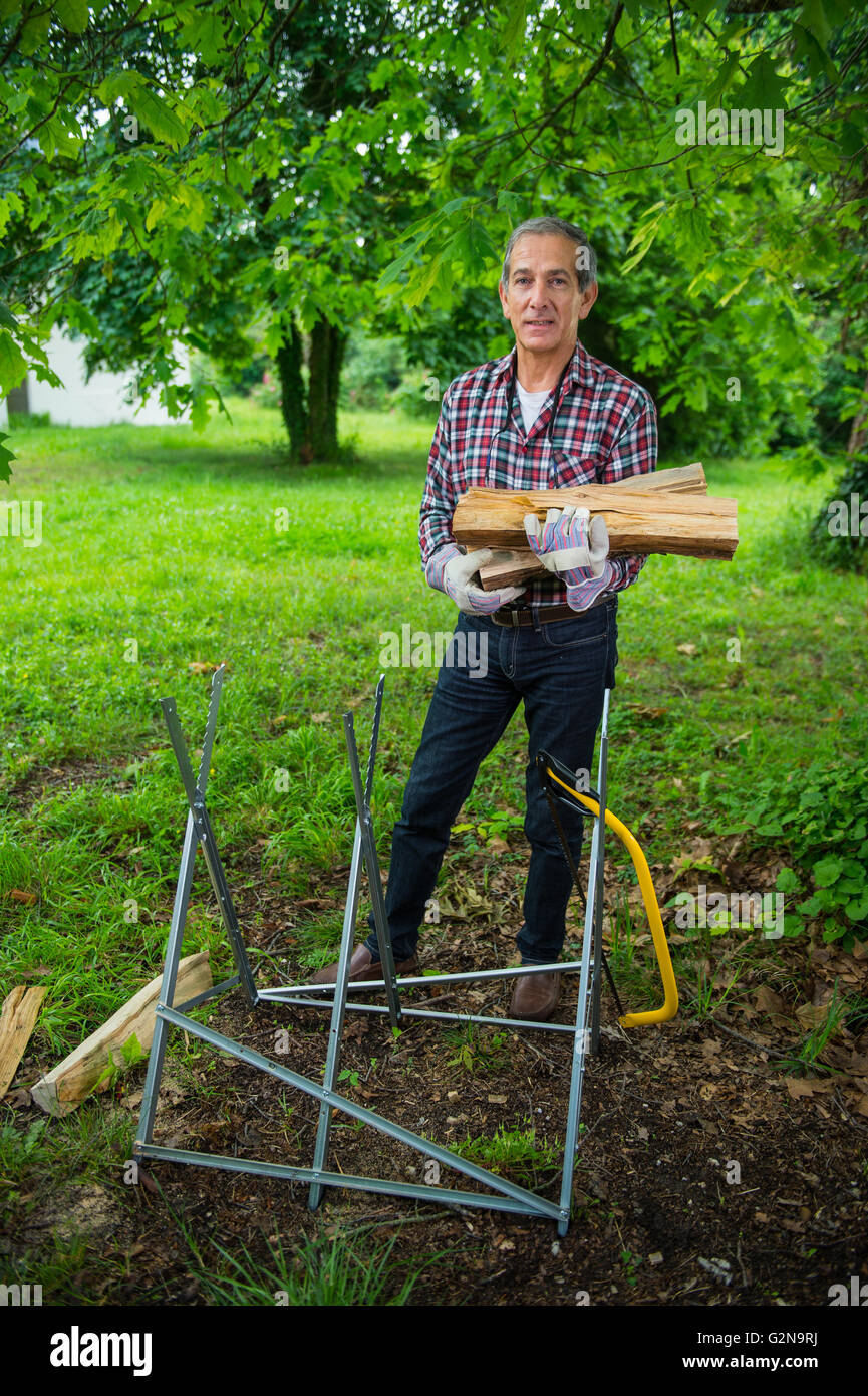 Senior-Mann trägt in seinen Armen das Brennholz sah er nur. Stockfoto