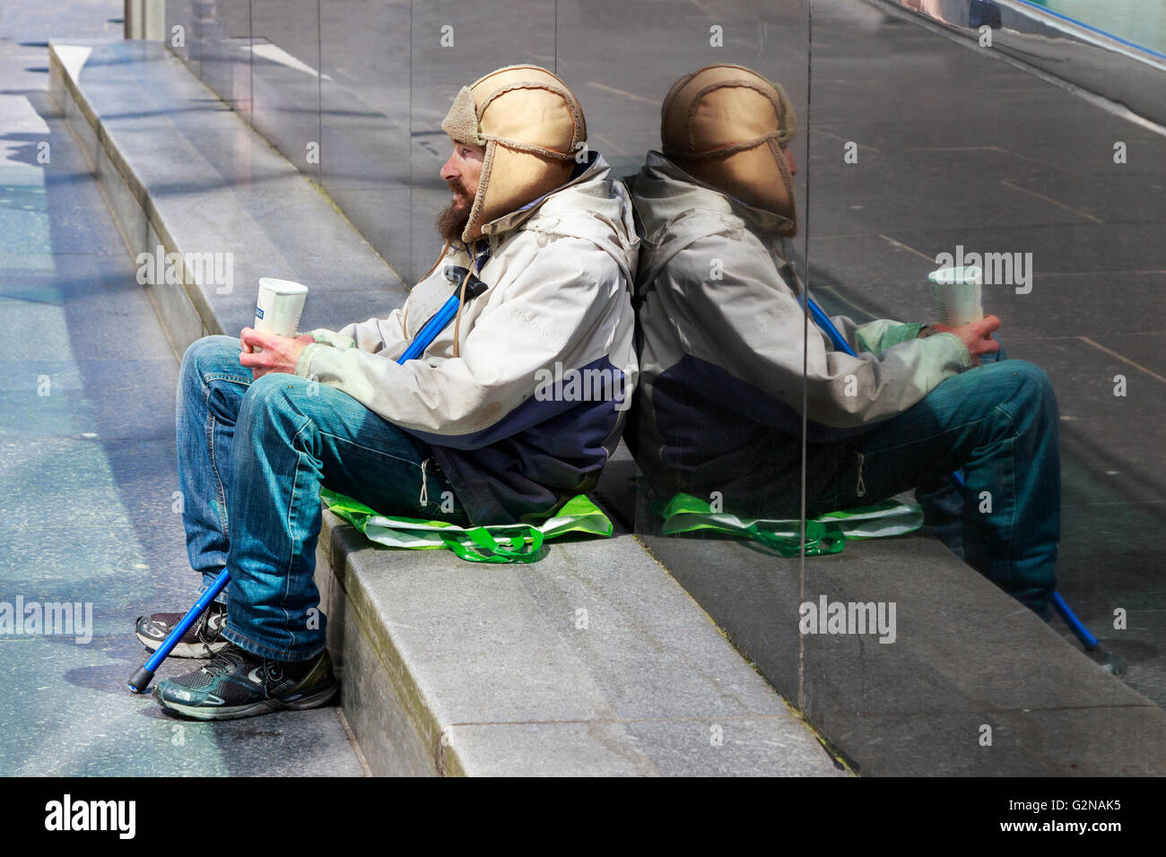 Mann betteln auf der Straße eine Sitzung gegen eine reflektierende gestylten Marmorwand, Glasgow, Schottland, UK Stockfoto