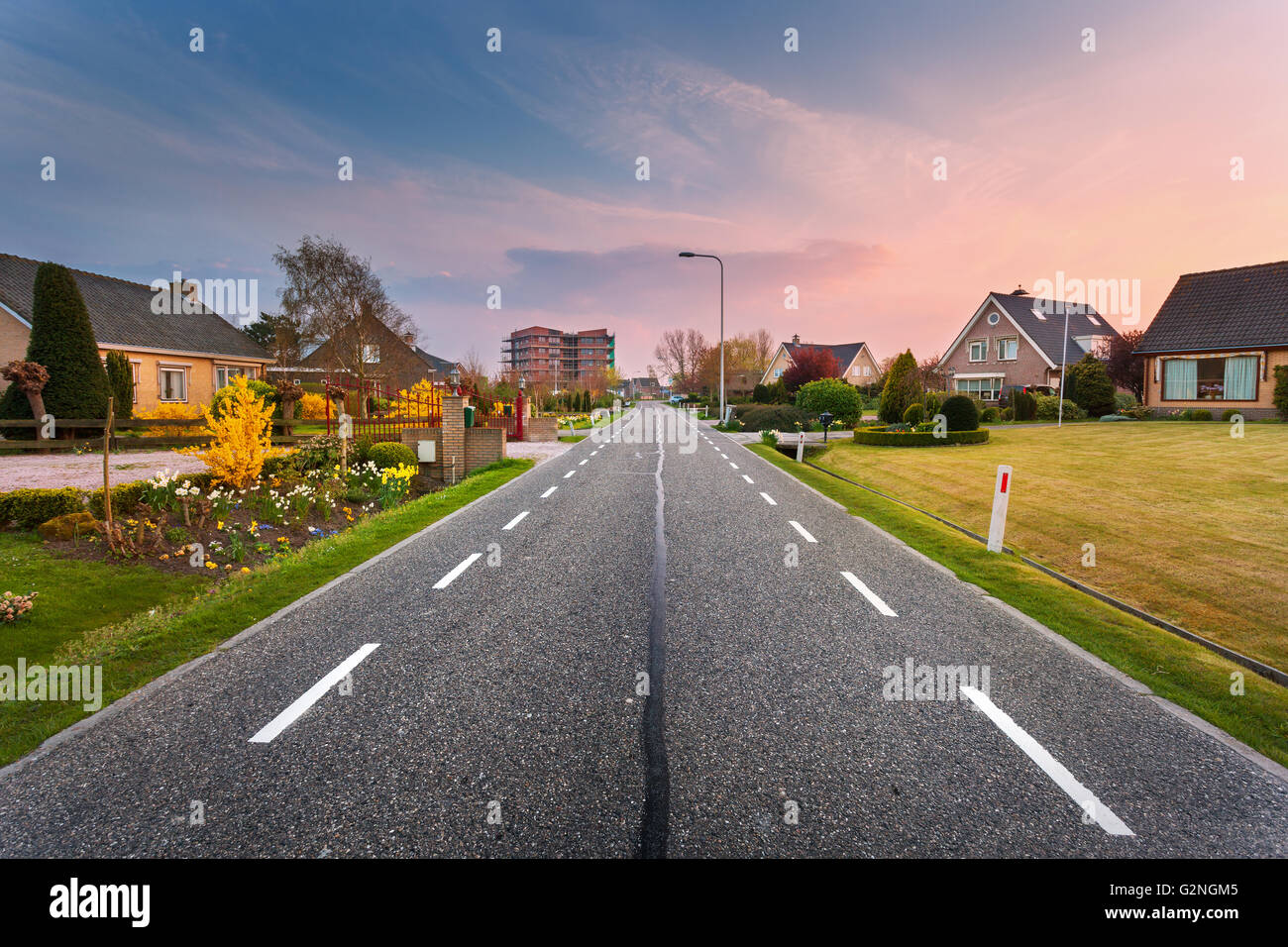 Schöne Landschaft mit europäischen asphaltierte Straße durch die Stadt mit Häusern und Höfen bei Sonnenuntergang in Niederlande. Ländliches Motiv Stockfoto