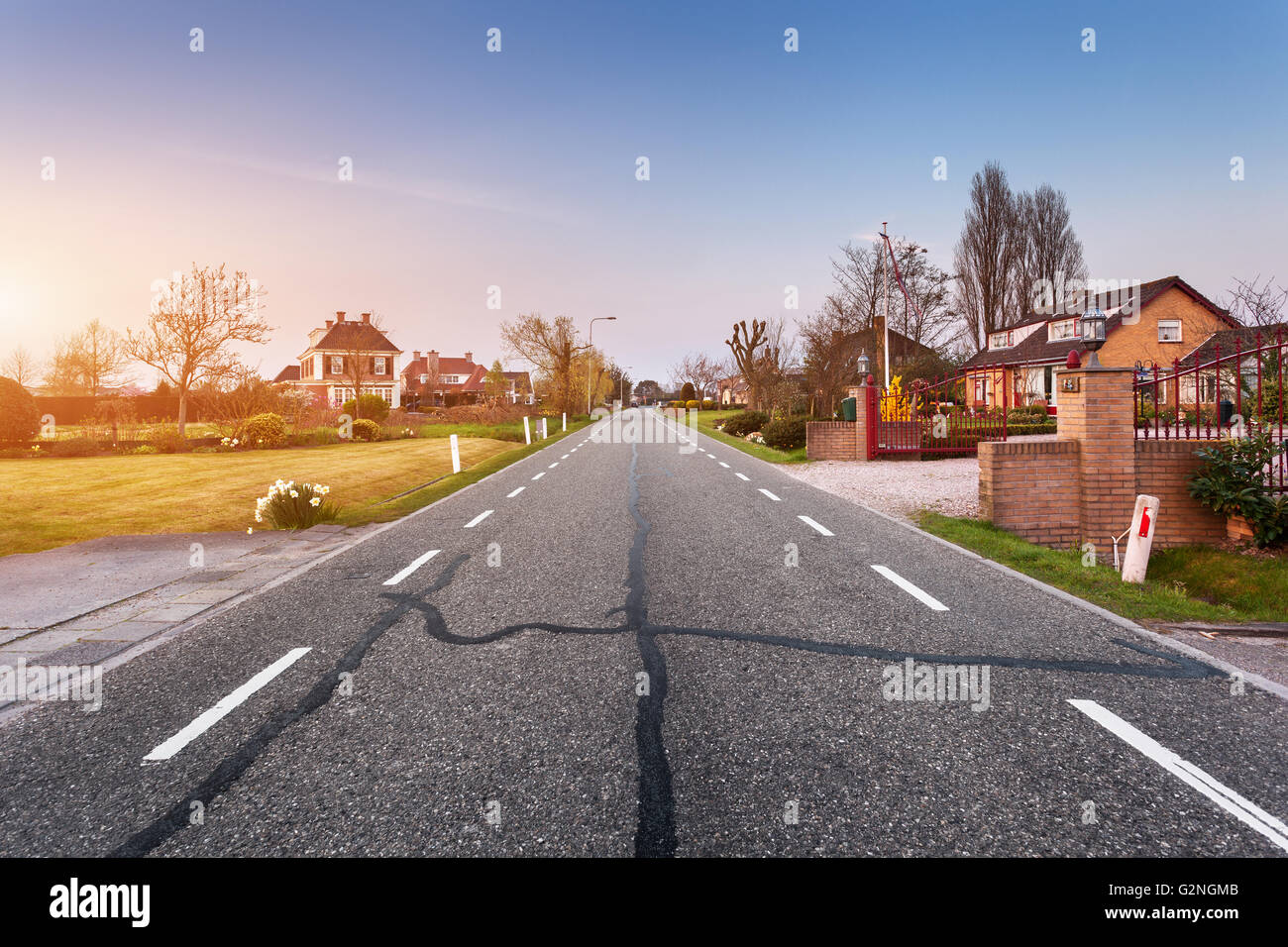 Schöne Landschaft mit europäischen asphaltierte Straße durch die Stadt mit Häusern und Höfen bei Sonnenuntergang in Niederlande. Ländliches Motiv Stockfoto