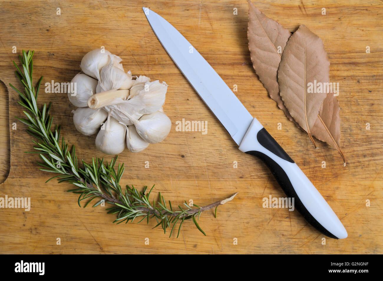 Knoblauch, Rosmarin und Lorbeer auf einer hölzernen Oberfläche mit einem Messer. Kochen und Hintergründe Stockfoto