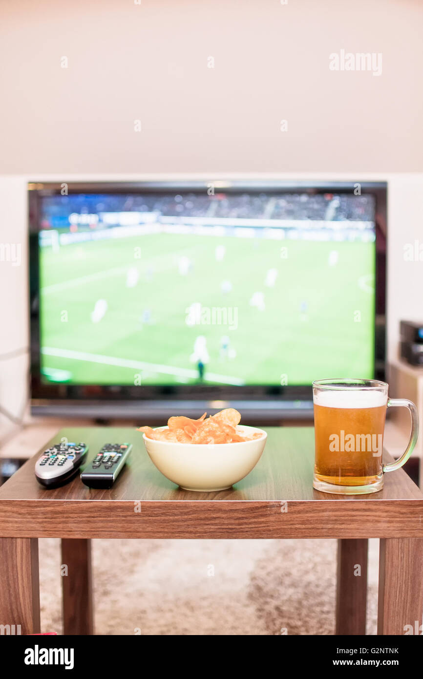 Bier, Chips und Fernbedienungen auf dem Tisch (im Hintergrund TV - Fußball-Spiel) Stockfoto