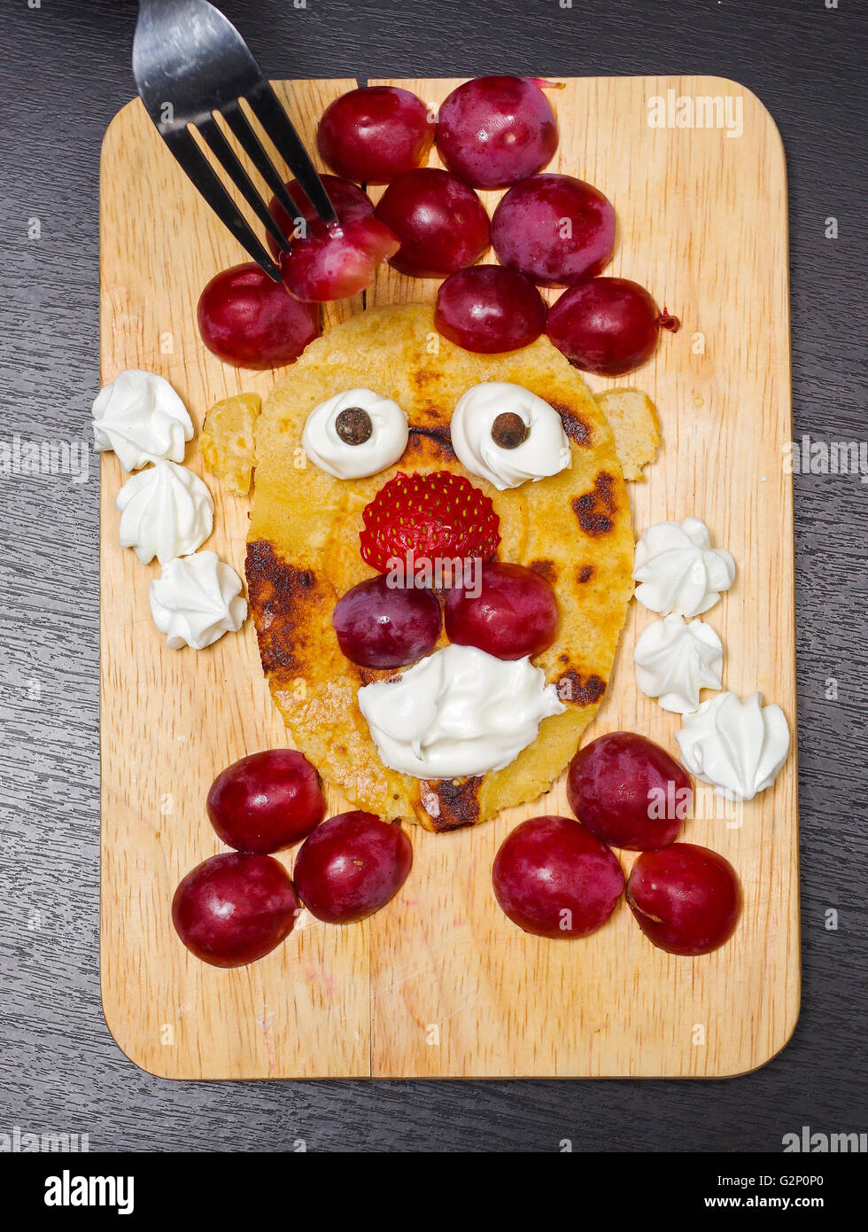 Lustig aussehenden Gesicht geschnittenen Trauben, Erdbeeren und Pfannkuchen, gemacht, von oben gesehen Stockfoto