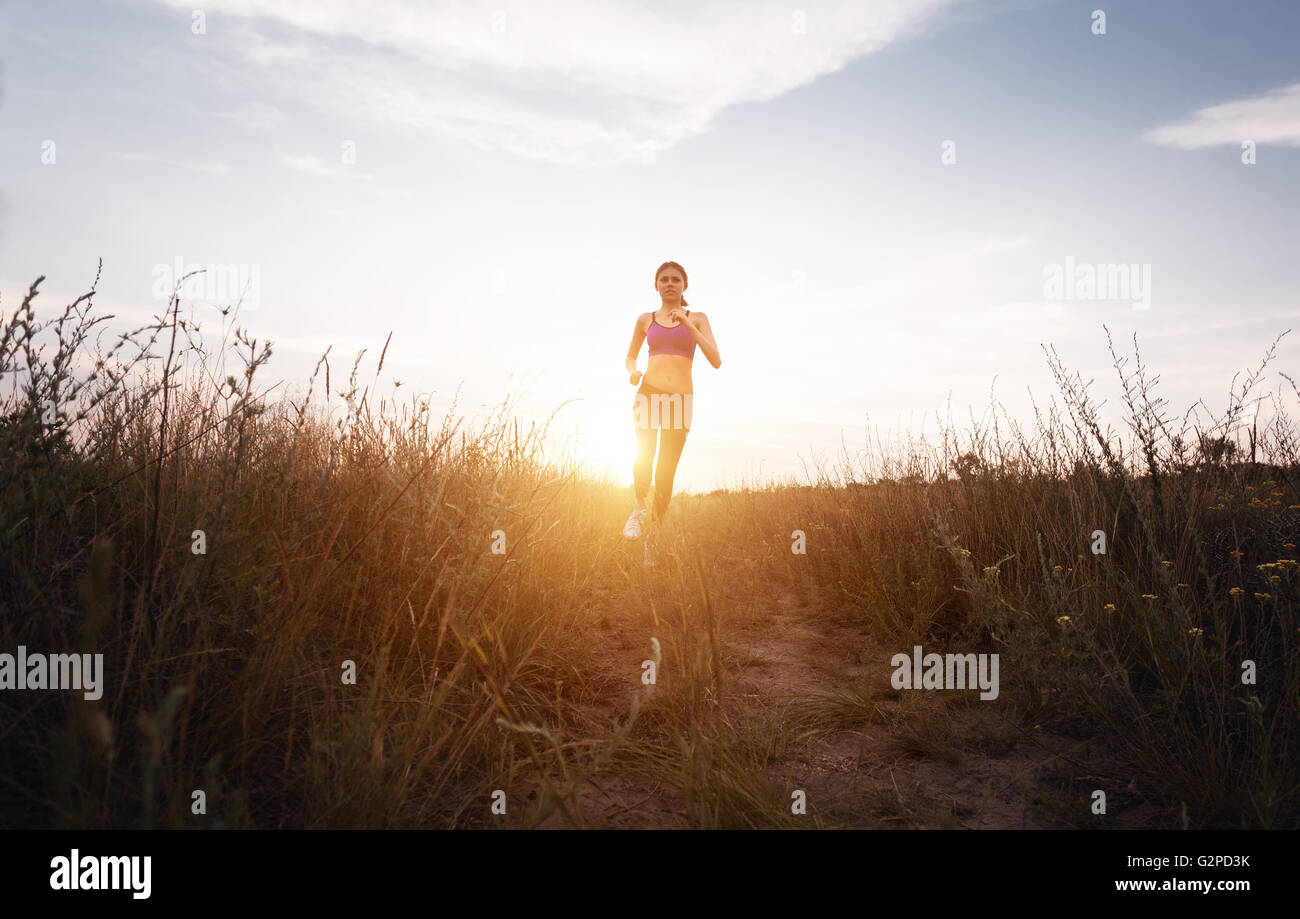 Sportliche Mädchen laufen auf einer Landstraße bei Sonnenuntergang in Sommerwiese. Lifestyle-Sport-Hintergrund Stockfoto