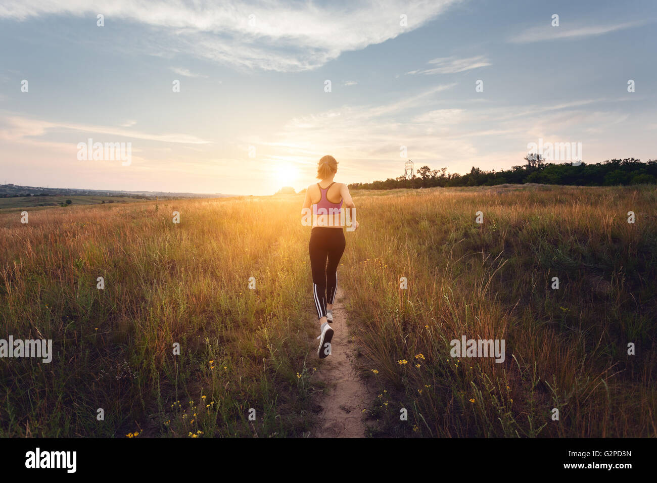 Sportliche Mädchen laufen auf einer Landstraße bei Sonnenuntergang in Sommerwiese. Lifestyle-Sport-Hintergrund Stockfoto