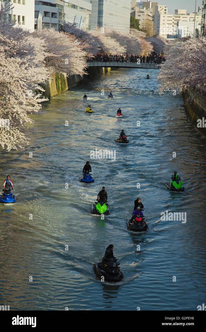 Japan, Tokyo, Meguro Fluss Menschenmenge auf Brücke Kirschbäume sichtbar an beiden Ufern des Flusses anzeigen, fahren Jet-Skis auf dem Fluss. Stockfoto