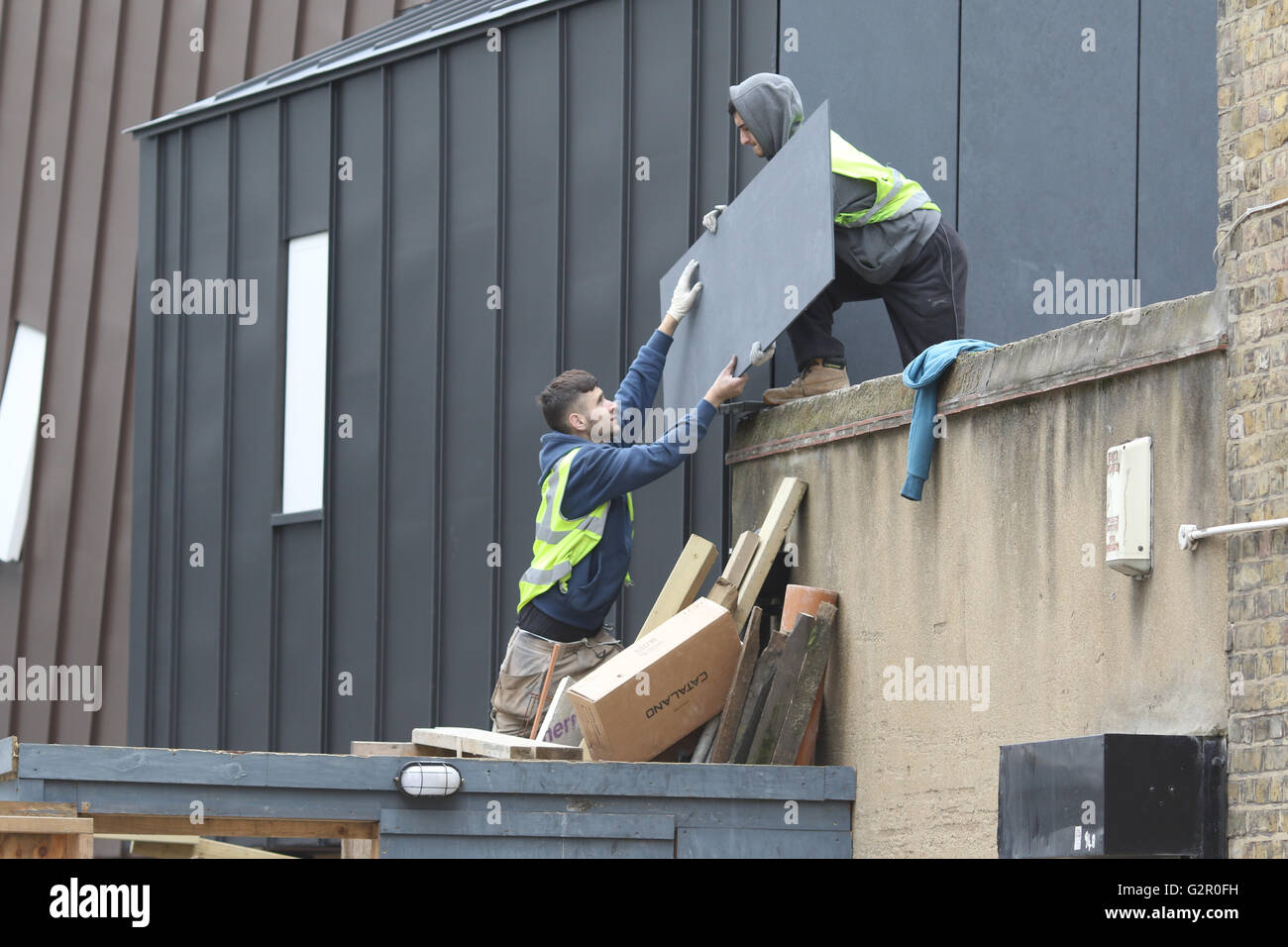 Bauarbeiter heben eine Holzplatte über eine Mauer Stockfoto