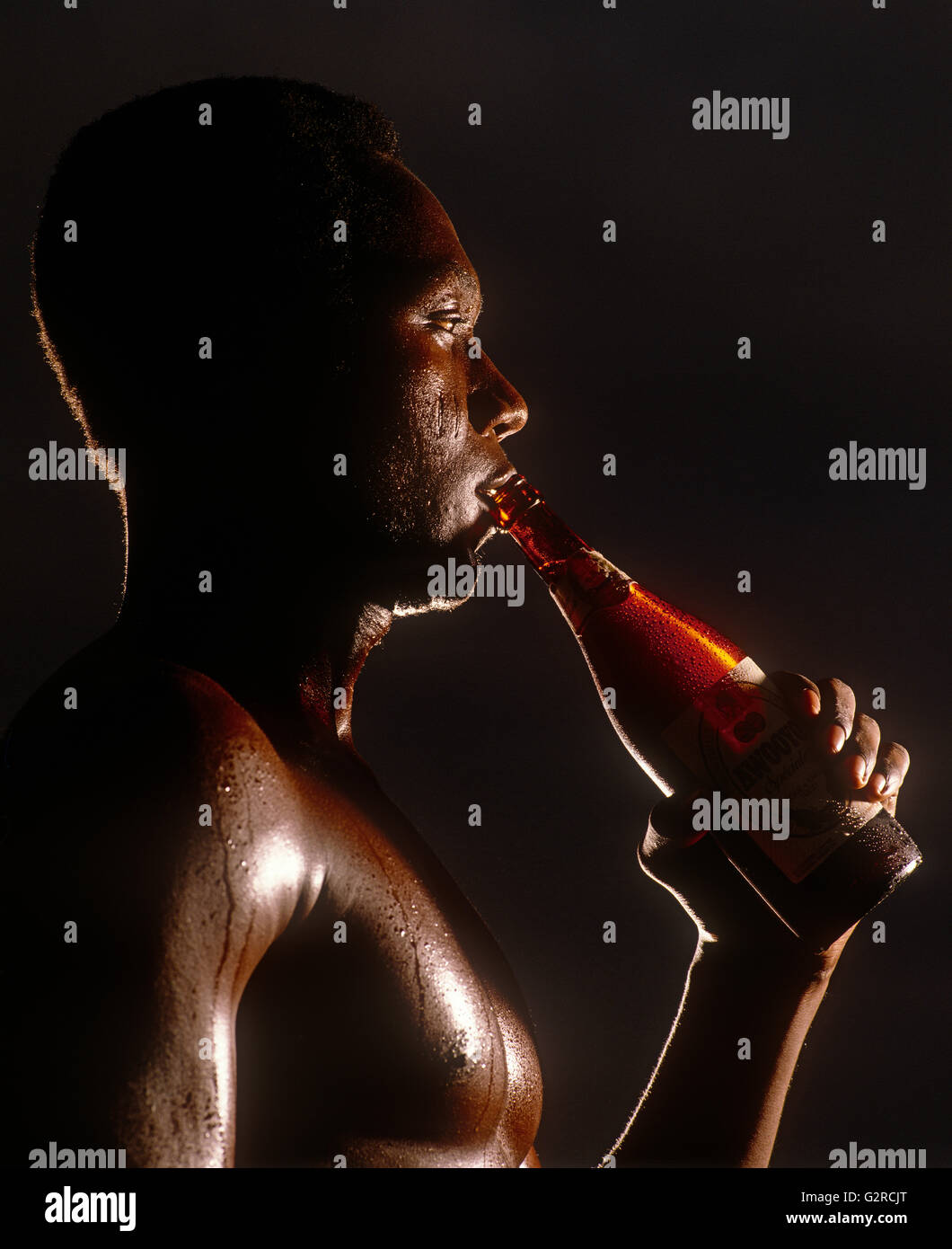 Ein Mann trinkt eine Flasche Alkohol, drinnen. Stockfoto